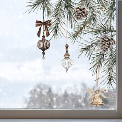 Three rustic Christmas ornaments hanging from pine tree branches in front of a snowy window. The ornaments include a brown ribbed glass ball with a brown bow, a clear glass teardrop, and a gold bell with a white bow.