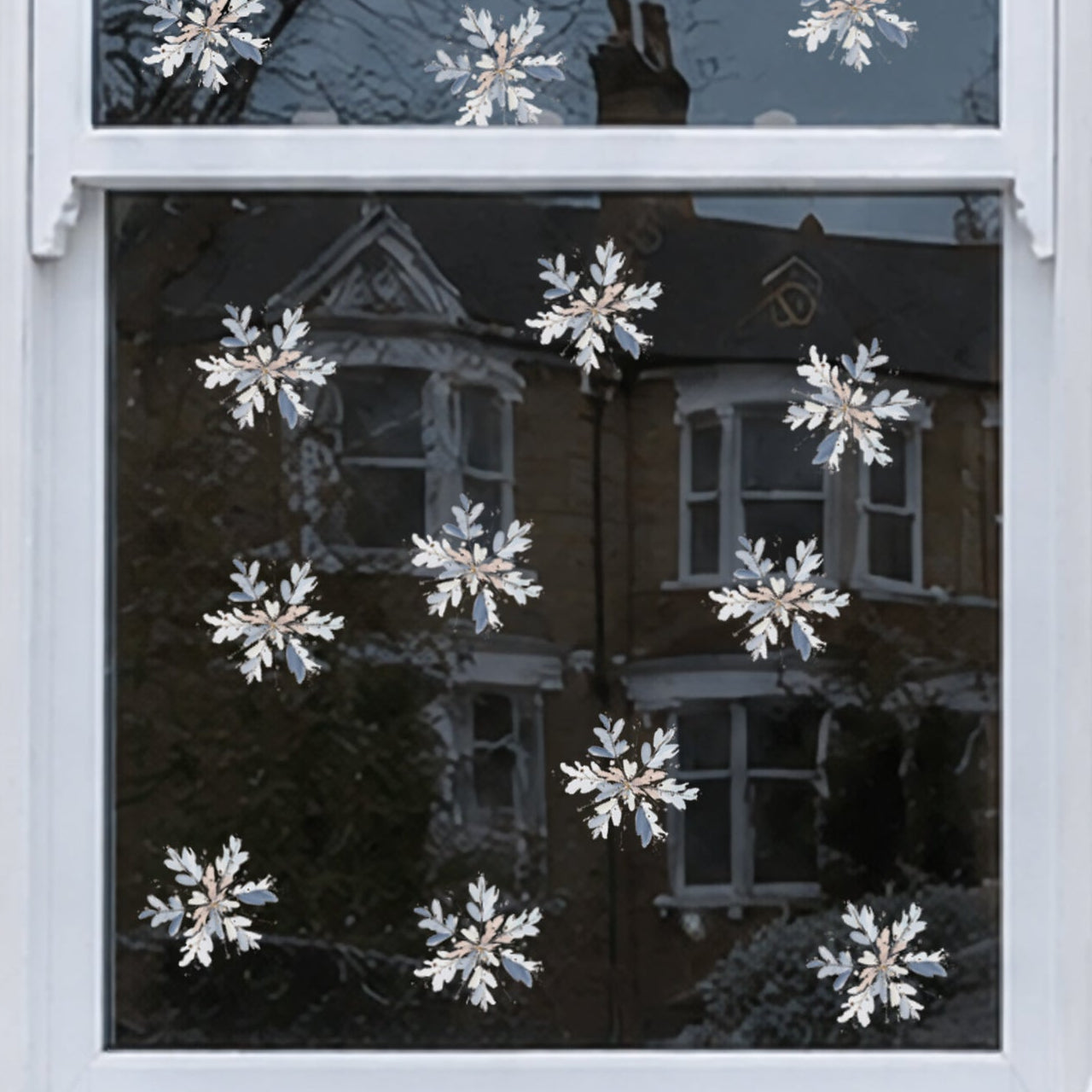 White snowflake window decals applied to a white-framed window on a brick house exterior, with snow on the sill and reflections of neighboring houses visible in the glass.