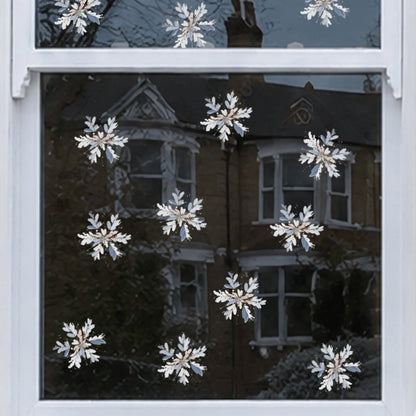 White snowflake window decals applied to a white-framed window on a brick house exterior, with snow on the sill and reflections of neighboring houses visible in the glass.